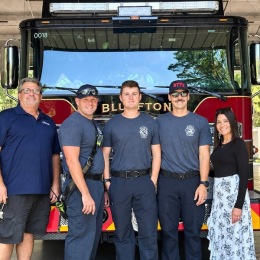 a woman standing with fire fighters in front of a fire truck